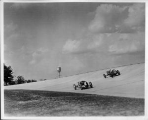 Packard Co. file photograph of two 1928 Packard race cars on track at proving grounds. Inscribed on photo back: "Packard Motor Car Co. Proving Grounds 2.5 mile concrete speedway, Utica, Mich., inauguration ceremonies 14 June 1928; Leon Duray, 91-cubic inch front drive Miller special #4, & Norman Batton, #22, coming out of curve at 140-mph."
