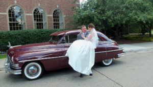 A groom carrying his bride out of a 1949 Packard