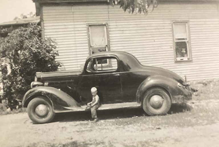 A little boy sitting on the running board of the 1937 Packard Eight Coupe