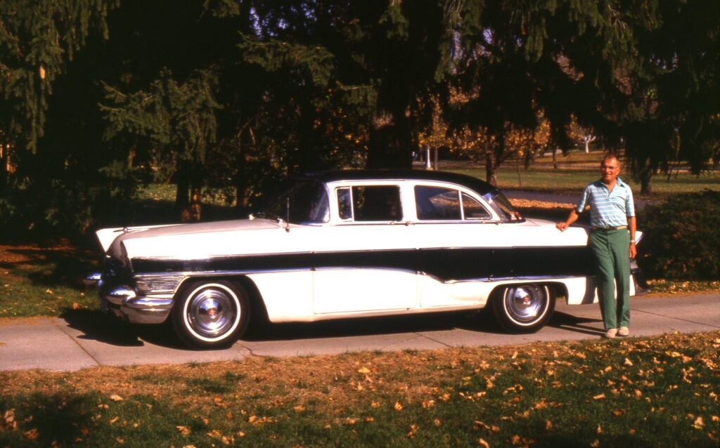 White and black Packard with a man standing next to it