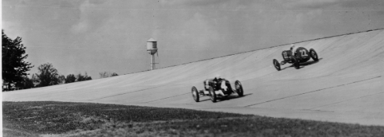 Packard Co. file photograph of two 1928 Packard race cars on track at proving grounds. Inscribed on photo back: "Packard Motor Car Co. Proving Grounds 2.5 mile concrete speedway, Utica, Mich., inauguration ceremonies 14 June 1928; Leon Duray, 91-cubic inch front drive Miller special #4, & Norman Batton, #22, coming out of curve at 140-mph."